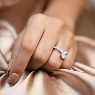 a woman's hand placed on a golden silk cloth with her wearing a white gold lab grown diamond solitaire ring on her ring finger