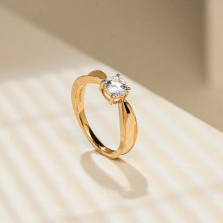 yellow gold lab grown diamond engagement ring placed on a beige coloured surface with light shining on it