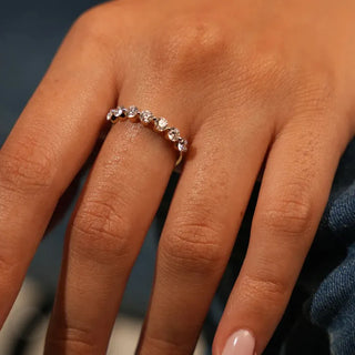 a woman's hand placed on a blue surface with a white gold lab grown diamond eternity band on her middle finger