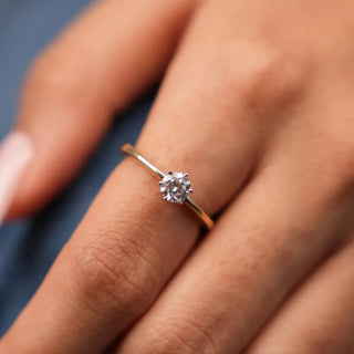 a woman wearing a yellow gold lab grown diamond engagement ring on her index finger placed on a light blue surface
