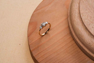 Yellow gold three-stone ring with lab-grown diamonds in a prong setting, resting on a smooth wooden surface.