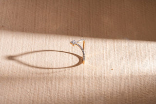 A gold chevron V-ring with pavé lab-grown diamonds stands upright on a textured, light wood-grain surface.