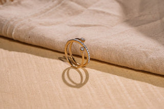 A yellow gold double-band ring with pavé lab-grown diamonds and two small solitaires rests on beige fabric.