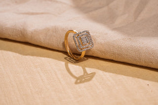 Gold ring with a square-shaped lab-grown diamond cluster setting, photographed on a beige textile background