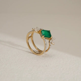 yellow gold lab grown diamond designer ring with a green gemstone placed with an off-white background