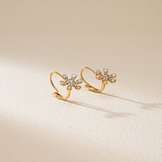 Pair of yellow gold flower-shaped hoop earrings with small lab grown diamonds on a light beige background.