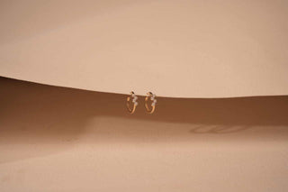 Pair of small yellow gold hoop earrings, each set with a cluster of four lab-grown diamonds, hanging from a curved light beige surface.