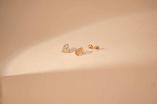 Yellow gold stud earrings with a curved, geometric shape and pavé-set lab-grown diamonds, displayed with both backs on a light beige surface.