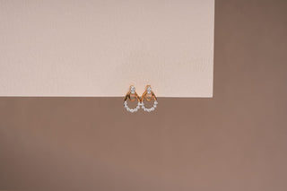 Pair of rose gold huggie earrings with a double-hoop design and pavé-set lab-grown diamonds, hanging from a two-toned beige surface.