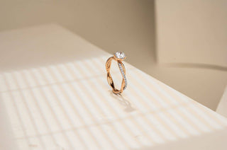 Rose gold ring with a round solitaire lab-grown diamond and a pavé-set braided band, displayed on a white illuminated surface