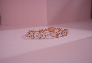 Rose gold bangle featuring pear and marquise-cut lab-grown diamonds in a floral pattern, lying on a light pink surface.