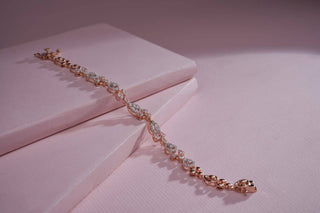"A delicate gold bracelet adorned with sparkling clear stones arranged in an intricate, alternating pattern, placed on soft pink surfaces with gentle lighting creating subtle shadows."
