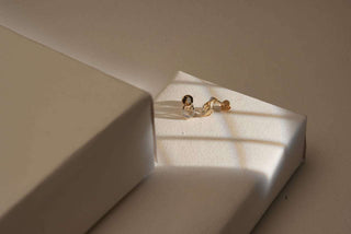 Minimalist gold earrings from Réia Diamonds displayed on a white platform, bathed in warm natural light with soft shadows