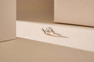 Two-tone ring with a flower-shaped pavé cluster of lab-grown diamonds and swirl accents, resting on a light beige surface with shadows.