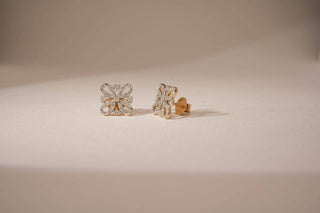 A pair of gold stud earrings with square-shaped floral diamond clusters, displayed on a light surface.