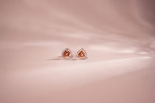 Two-tone stud earrings with a triangular design, featuring a rose gold center and pavé white lab-grown diamonds, resting on a soft pink background.