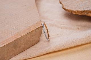 A delicate gold ring adorned with small white stones, standing upright against a rustic terracotta block on a soft beige fabric background with earthy tones.