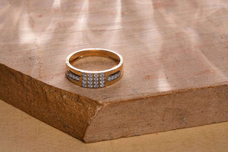 A close-up of a gold ring with two rows of diamonds, resting on a textured, light brown stone surface.