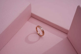 Gold band ring with small diamonds placed on a pastel pink geometric background