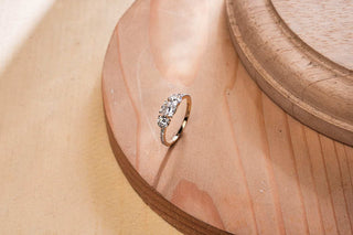 Réia lab-grown diamond engagement ring with three-stone setting in gold, displayed on wooden surface with soft beige backdrop.