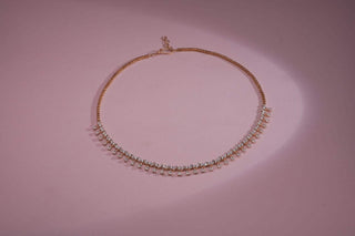 "Elegant gold necklace with a row of small white stones, displayed on a pink background"