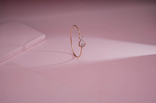 Minimal gold bangle with a circular diamond charm, displayed on a soft pink background.