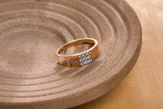 Gold ring with a square diamond-studded design, placed on a textured brown ceramic plate.