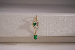 Elegant gold earring with diamond accents and green gemstone drops, displayed on a white textured surface.