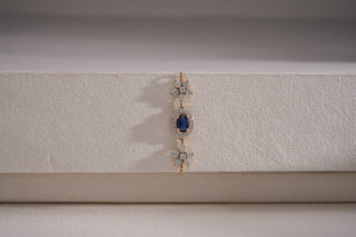 Réia lab-grown diamond pendant with oval blue gemstone centerpiece and floral diamond accents, displayed on a textured white surface.