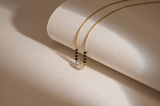 Réia lab-grown diamond mangalsutra featuring an oval diamond pendant with accent beads on a gold chain over beige backdrop.