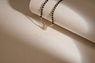 Réia lab-grown diamond mangalsutra with black bead chain and gold diamond pendant on beige textured background.