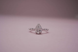 A pear-shaped lab-grown diamond on a white gold twisted band is displayed on a light pink background.