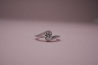 white gold lab-grown diamond engagement ring placed in the center of the frame with a light pink and grey background