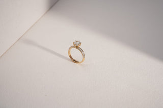 yellow gold lab-grown diamond engagement ring placed beside a white sheet with a white and grey background 