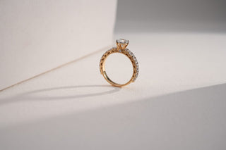 An ornate gold engagement ring with a lab-grown diamond band and a central solitaire stands against a white background.