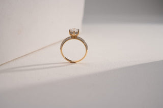 A yellow gold ring with a round solitaire lab-grown diamond and pavé band stands against a white background.