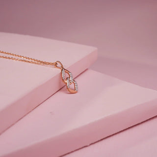 A rose gold necklace with a double interlocking link pendant featuring pave lab-grown diamonds rests on pink blocks.
