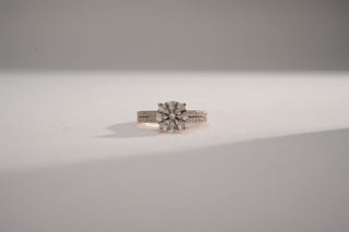 A white gold ring with a large, round central lab-grown diamond and double pavé diamond bands rests on a white surface.