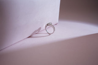 A white gold ring with a pave lab-grown diamond band and a crossover design stands on a pink surface.