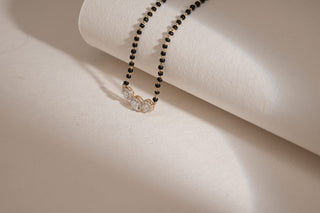 A mangalsutra with three round, linked lab-grown diamond cluster pendants rests on a white, curved surface