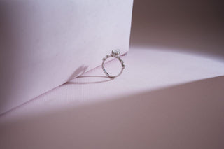 White gold solitaire ring with a lab-grown diamond and diamond-accented shank, on a white and gray surface.