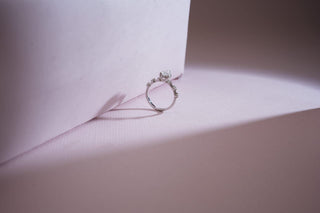 white gold lab-grown diamond engagement ring placed against a light pink sheet with a light pink and grey background