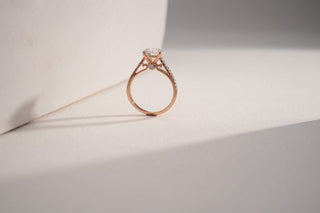 Rose gold solitaire ring with a large lab-grown diamond and diamond-pave shank, on a split white and gray background.
