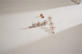 Rose gold floral dangle earrings with lab-grown diamond flower clusters and teardrop accents, on a light beige surface.
