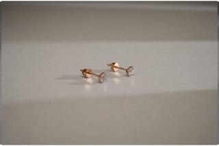 Pair of round lab-grown diamond stud earrings in four-prong rose gold basket settings with screw-backs, on a smooth, white surface.