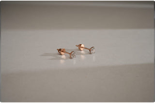 Pair of small, round lab-grown diamond stud earrings in three-prong rose gold basket settings with screw-backs on a light gray surface.