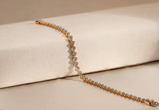 Yellow gold tennis bracelet featuring a full row of lab-grown diamonds with heart-shaped settings. Displayed on a beige riser.
