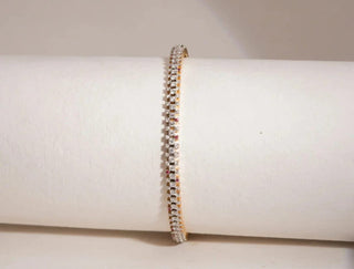 Three-row gold bracelet with lab-grown diamonds and pink gems, featuring a slightly larger center row. Displayed on a white cylinder.
