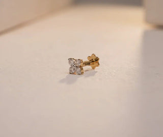 Close-up of a yellow gold nose pin with a lab-grown diamond flower cluster and star backing, on a light beige surface.