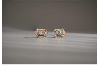  Pair of square stud earrings with a round lab-grown diamond center, featuring a swirling rose and white gold or diamond-pave setting. Displayed on a light gray surface with a diagonal shadow.